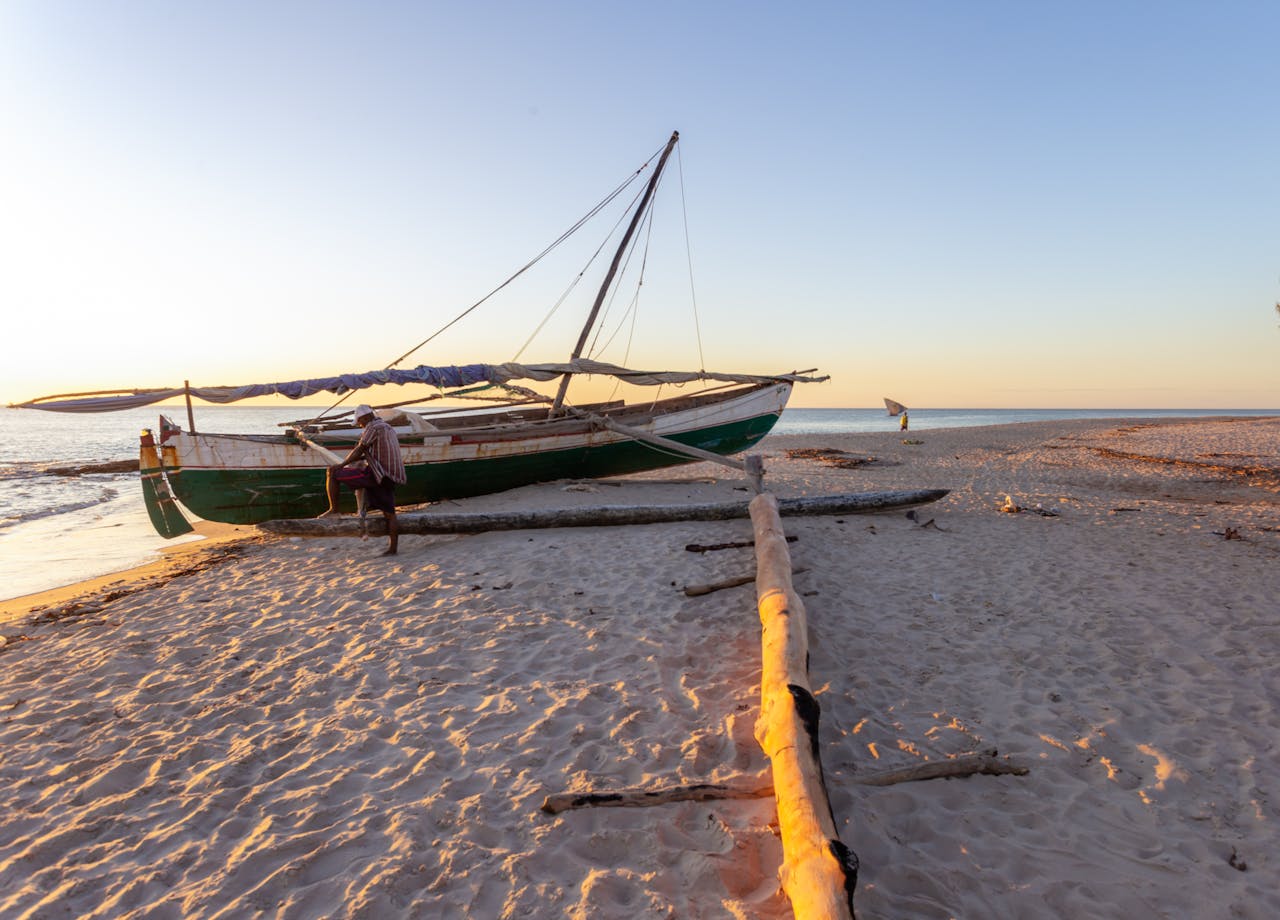 Home A serene beach scene in Madagascar with a traditional fishing boat during sunset on the sandy shore.